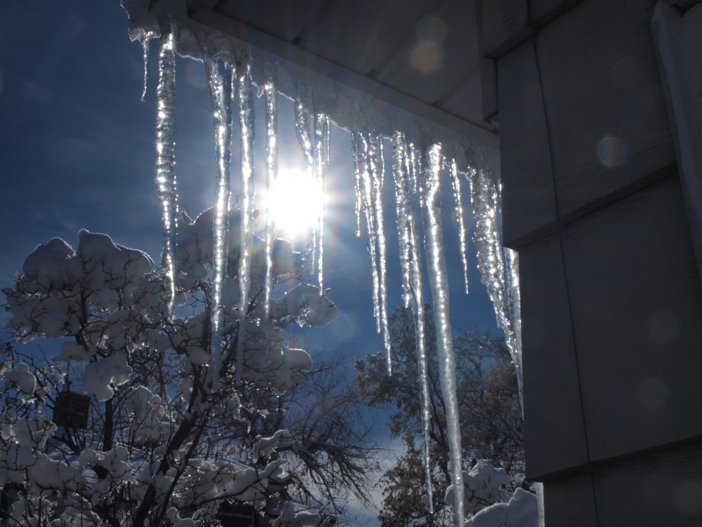 iciles hanging down with the sun flaring behind it