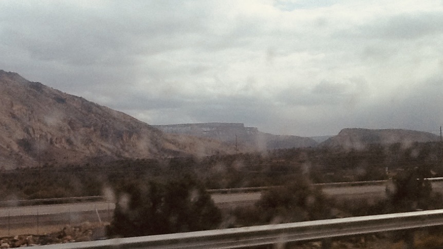 A cloudy sky in black white through a speeding car window with blurry mountains in the distance